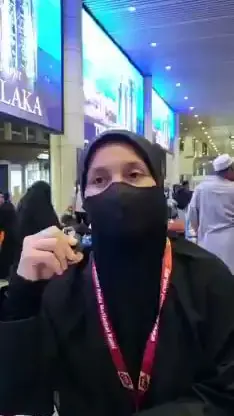 Jemaah wanita bertudung hitam bertali leher KRS Travel memberi testimoni di lapangan terbang