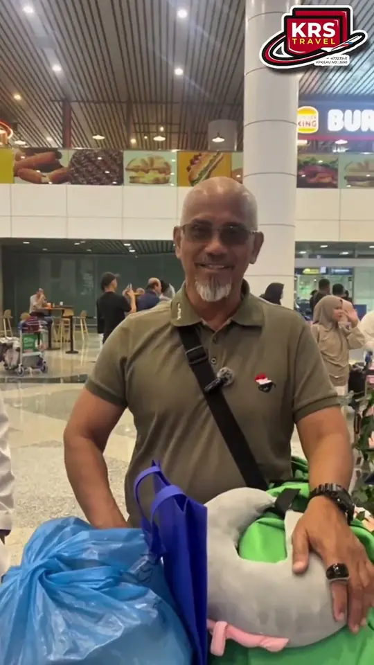 Jemaah lelaki berjanggut membawa beg tangan dan bantal perjalanan di lapangan terbang