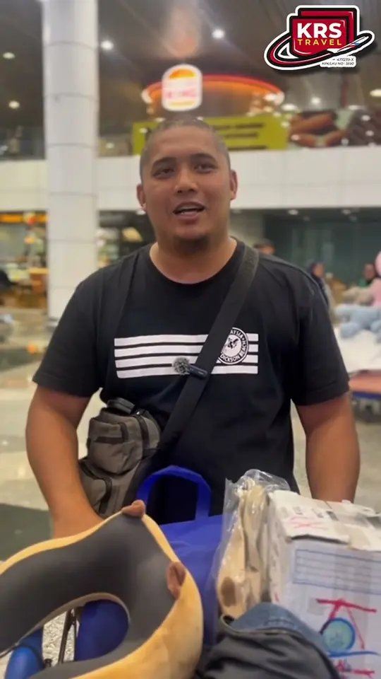 Jemaah lelaki berbaju hitam dengan beg sandang memberi testimoni di lapangan terbang