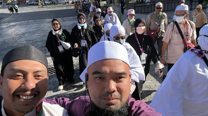 Dua petugas KRS Travel bergambar sambil mengiringi rombongan jemaah haji berjalan ke tapak ibadah musim haji 1446H