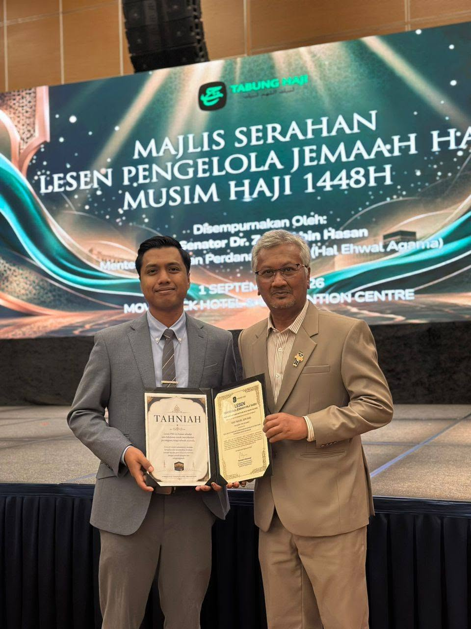 Dua peserta bergambar dengan sijil KRS Travel di hadapan latar Majlis Serahan Lesen PJH 1448H