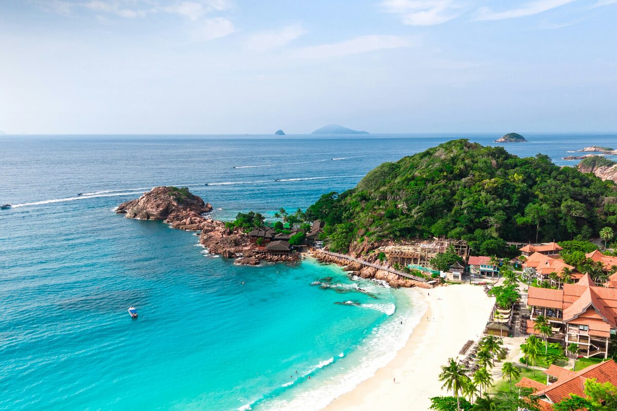 Pandangan udara teluk Pulau Redang — air pirus, pantai berpasir putih dan chalet resort berbumbung merah di tepi bukit berhutan, Terengganu — Pakej Pulau Redang KRS Travel
