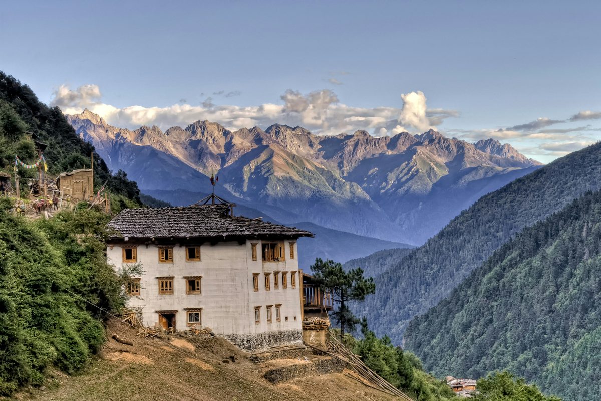 Rumah tradisional di lereng gunung dengan latar barisan puncak berbatu di Yunnan, China — Pakej Yunnan KRS Travel